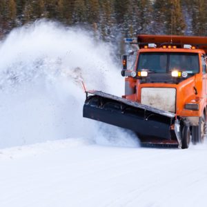Snow plow truck clearing road after winter snowstorm blizzard for vehicle access